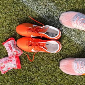 Overhead view of Datekin snack packs, orange football boots, and running trainers on grass—perfect for athlete recovery and breaking fast.